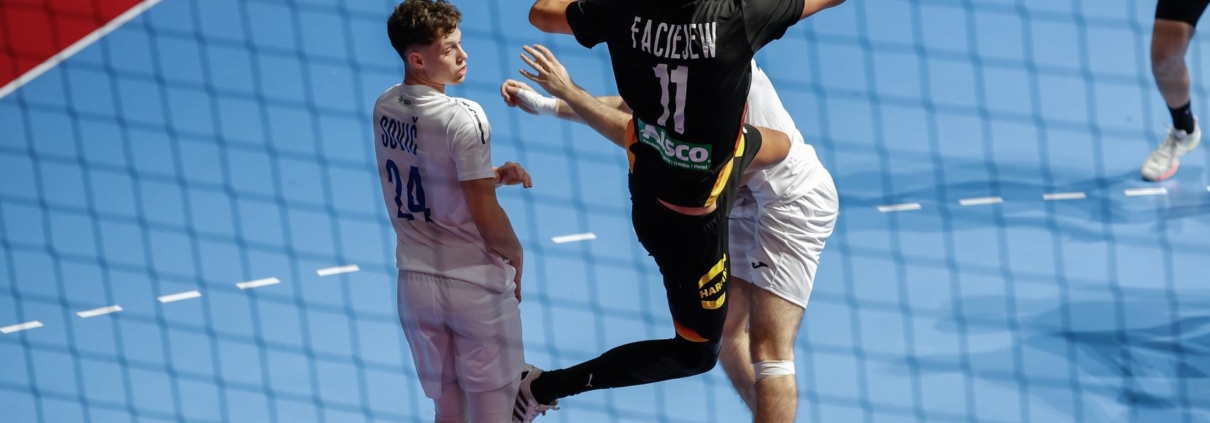 A player in a black jersey with the number 11 leaps to strike a ball during a handball match, while an opponent in a white jersey watches closely.