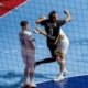 A player in a black jersey with the number 11 leaps to strike a ball during a handball match, while an opponent in a white jersey watches closely.